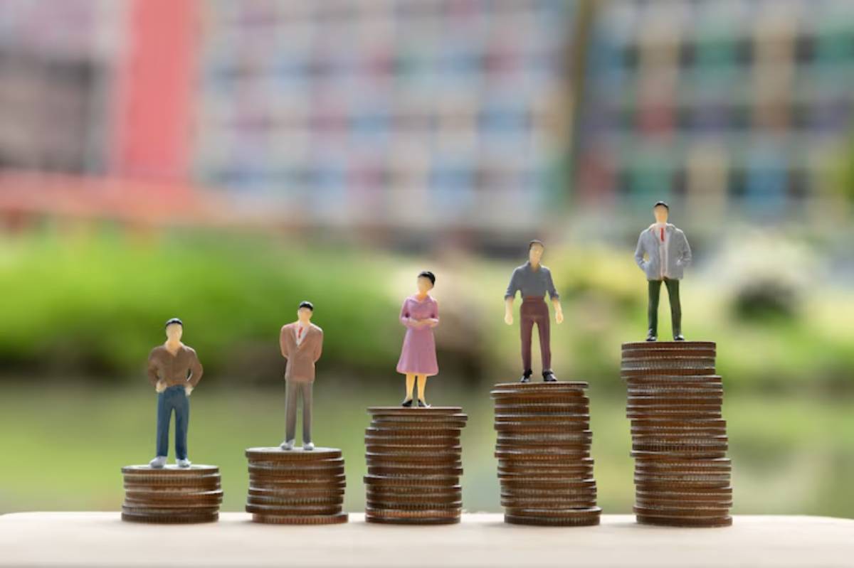 Five miniature figures stand on stacked coins, symbolizing growth and financial progress, against a blurred, colorful background.