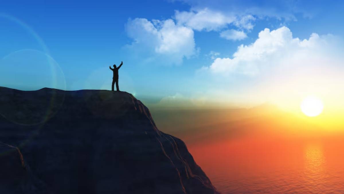 Silhouette of a person standing triumphantly on a cliff against a vibrant sunset with colorful clouds above the ocean.