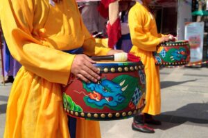 Two performers in vibrant yellow traditional attire hold decorative drums featuring intricate dragon and floral designs.