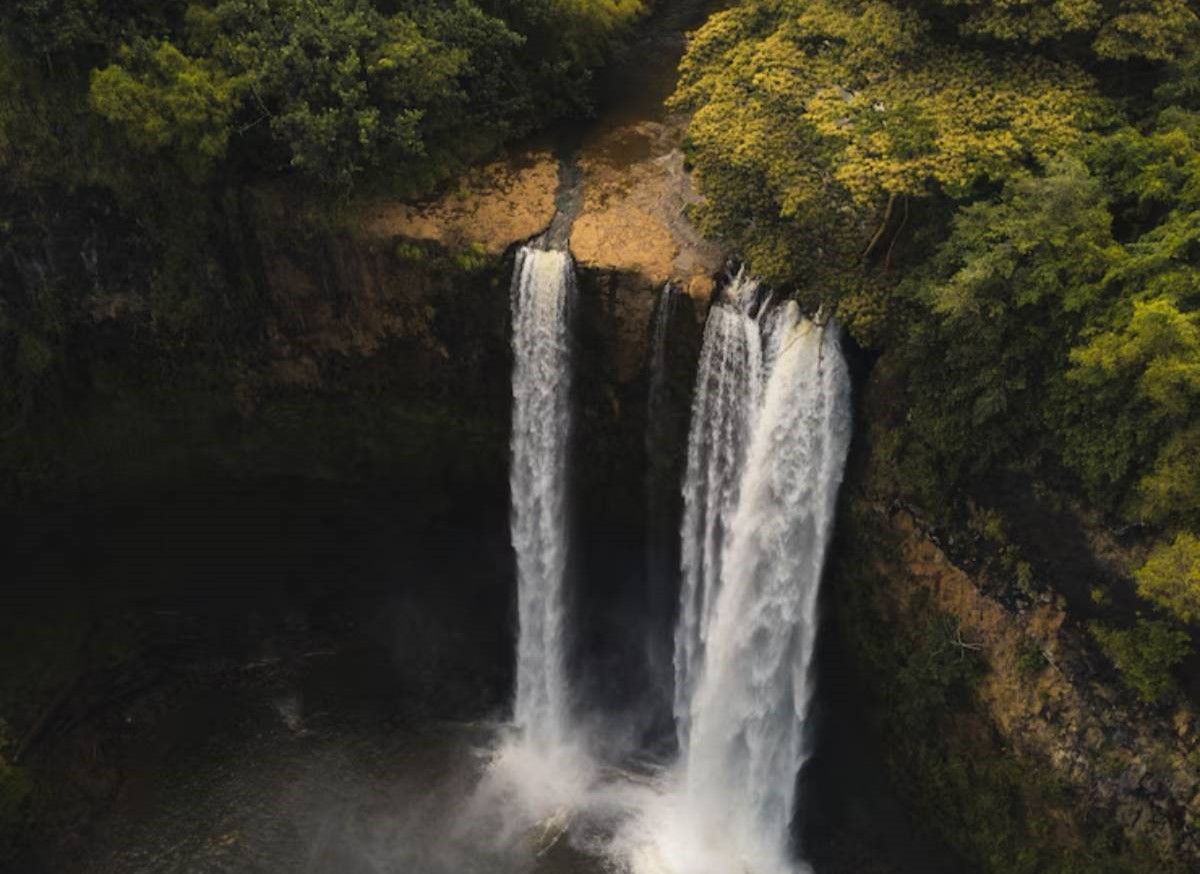 Aerial view of two cascading waterfalls surrounded by lush greenery and mist, plunging into a serene pool below.