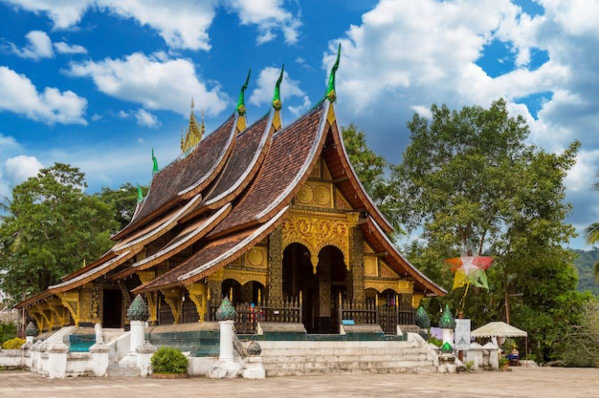 A beautifully ornate Lao temple with golden accents and traditional architecture, surrounded by lush greenery under a blue sky.