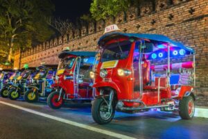 Colorful tuk-tuks lined up at night against a brick wall, showcasing vibrant lights and a lively urban atmosphere.