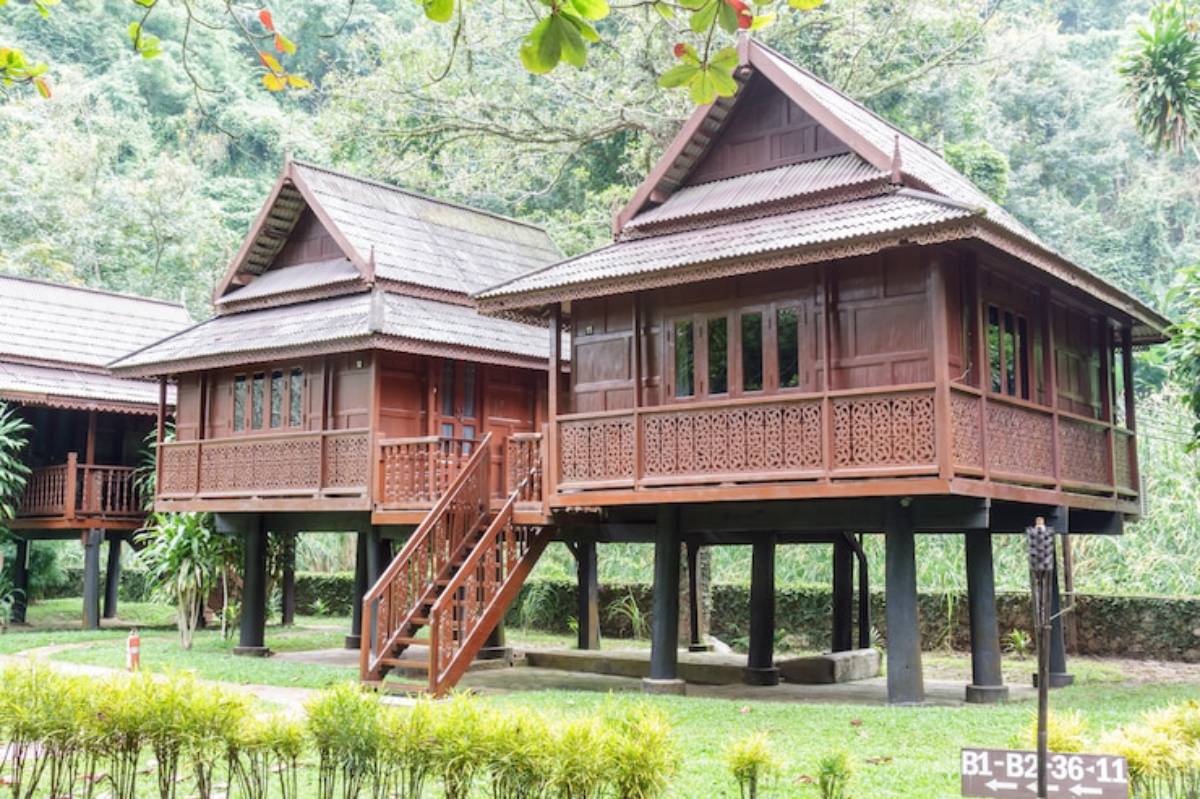 Two wooden, traditional houses on stilts surrounded by lush greenery, showcasing intricate carvings and staircases.
