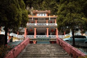 Stairs lead up to Gua Perak temple, adorned with red lanterns and surrounded by lush greenery and tall trees.