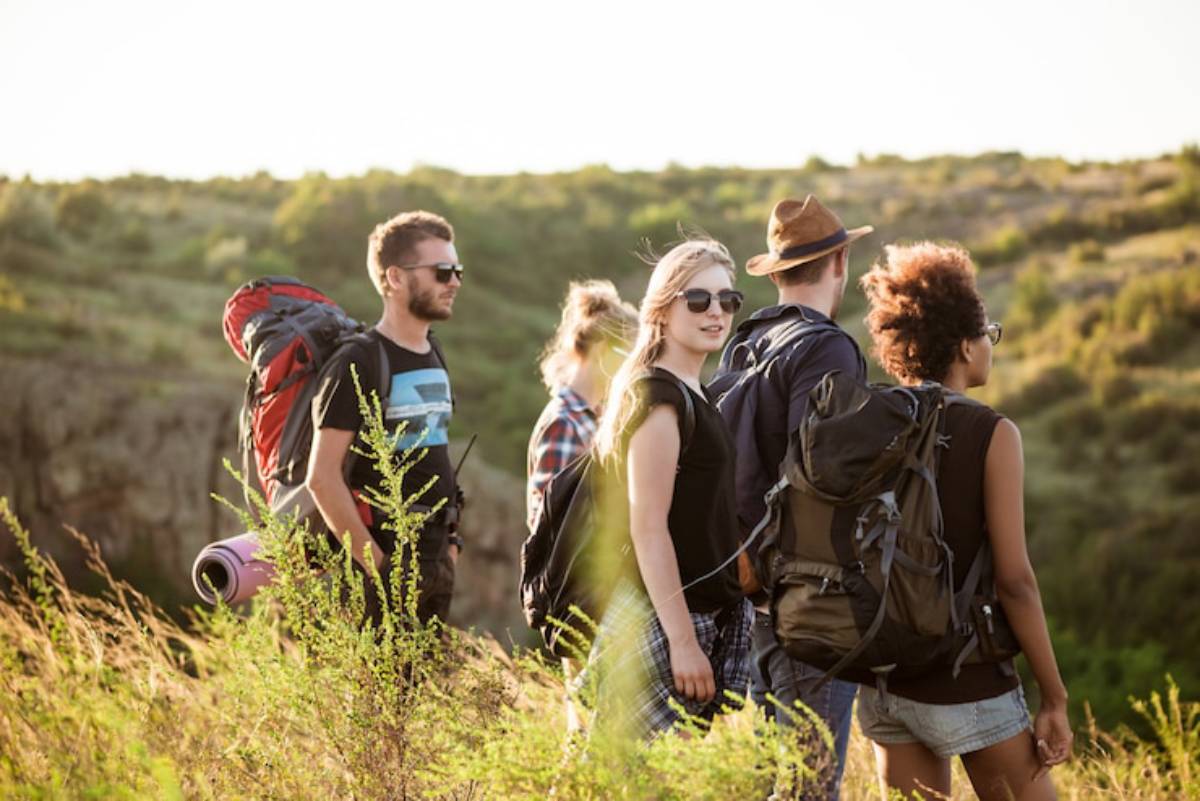 A group of five hikers stands together, backpacks on, overlooking a scenic landscape bathed in warm sunlight.