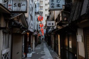 Narrow alleyway in a Japanese city, lined with illuminated lanterns and shop signs, showcasing an atmospheric, vintage charm.