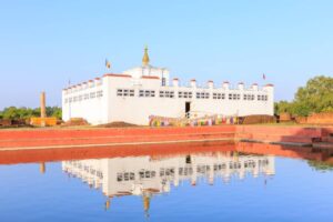 A serene white temple with a golden spire, reflecting in a calm pond, surrounded by greenery and traditional prayer flags.