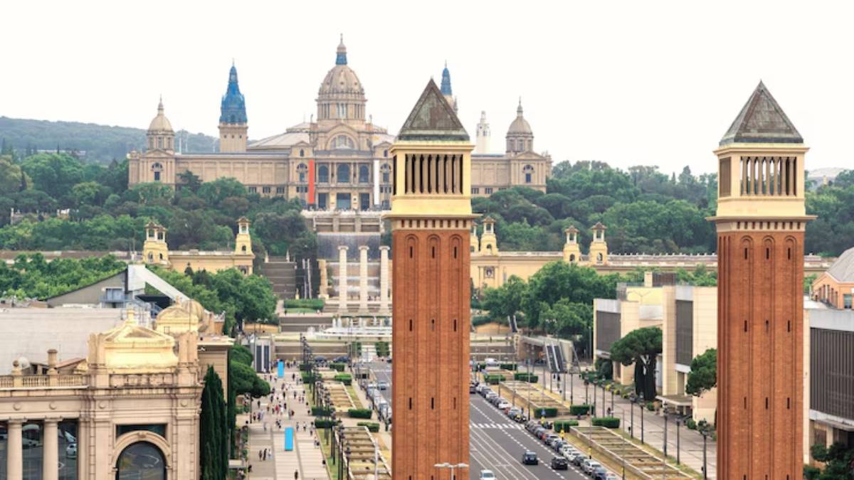 A view of Plaça d'Espanya in Barcelona, featuring iconic twin towers and the National Palace in the background, surrounded by greenery.