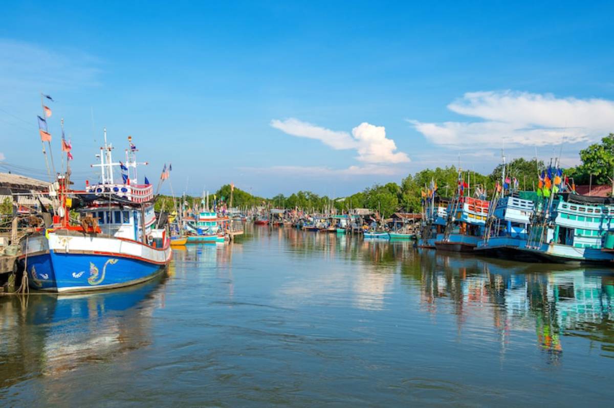 A serene river scene with colorful fishing boats lined along the banks under a clear blue sky, reflecting in the calm water.