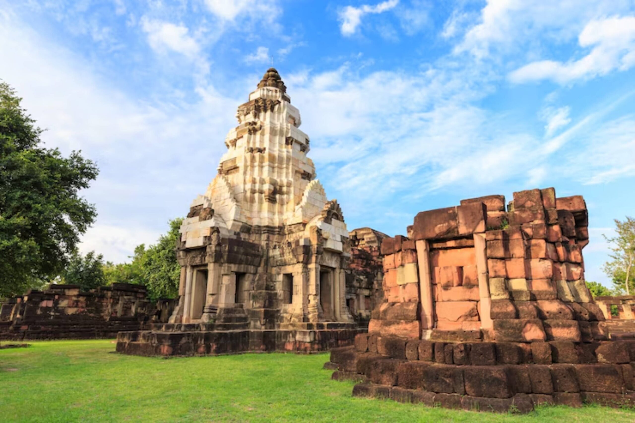 Ancient stone temple with a pyramidal structure surrounded by lush greenery and remnants of older architecture under a blue sky.