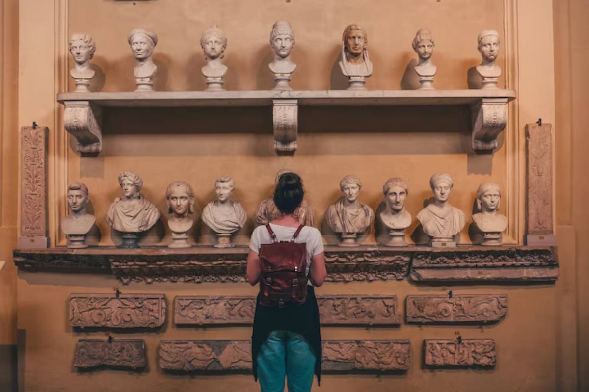 A person stands before a wall display of classical marble busts and ornate stone carvings, immersed in the art of a museum.