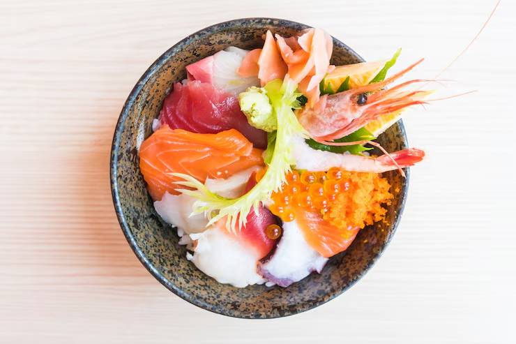 A colorful bowl of sushi, featuring assorted sashimi, shrimp, fish roe, pickled ginger, and garnish over rice.