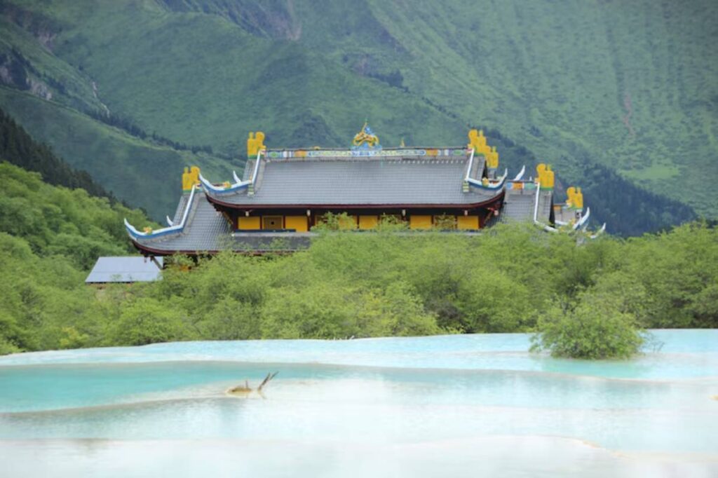 A vibrant temple nestled among lush mountains, with turquoise water in the foreground reflecting the serene landscape.