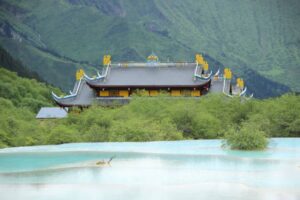 A vibrant temple nestled among lush mountains, with turquoise water in the foreground reflecting the serene landscape.