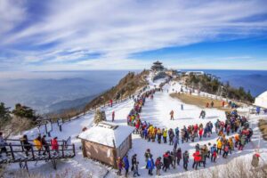 A bustling snowy mountain peak with crowds of tourists in colorful jackets, enjoying the panoramic views and clear blue sky.
