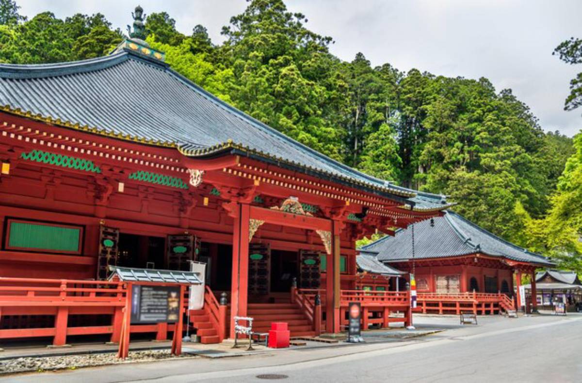 Two traditional red Japanese temples with green accents, surrounded by lush greenery and a clear blue sky.