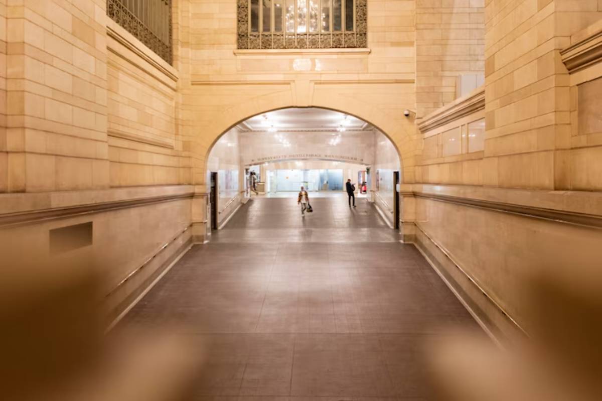 An empty corridor in a beautifully lit, historic building, showcasing tall arches and elegant architecture, with two people in view.