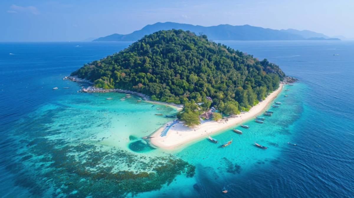 Aerial view of a tropical island with lush greenery, sandy beaches, and turquoise waters, dotted with boats along the shoreline.