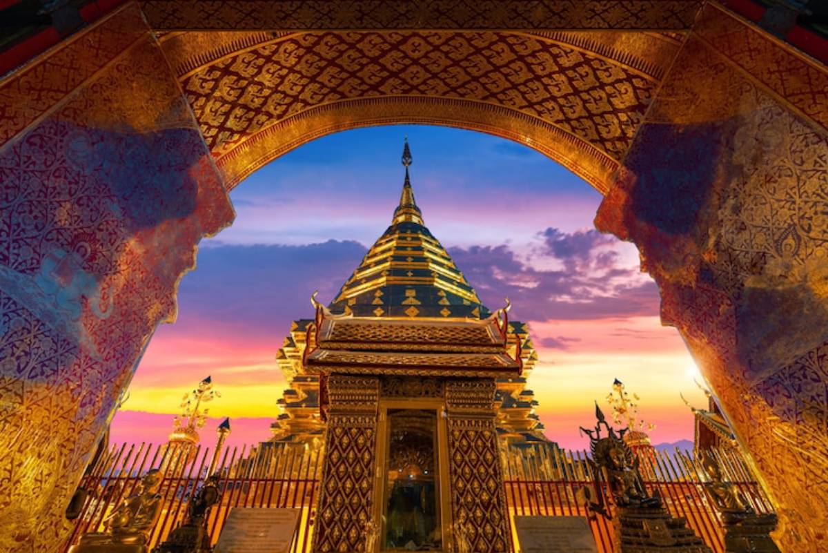 Golden temple spire framed by ornate archway at sunset, showcasing intricate details and vibrant hues of the sky.