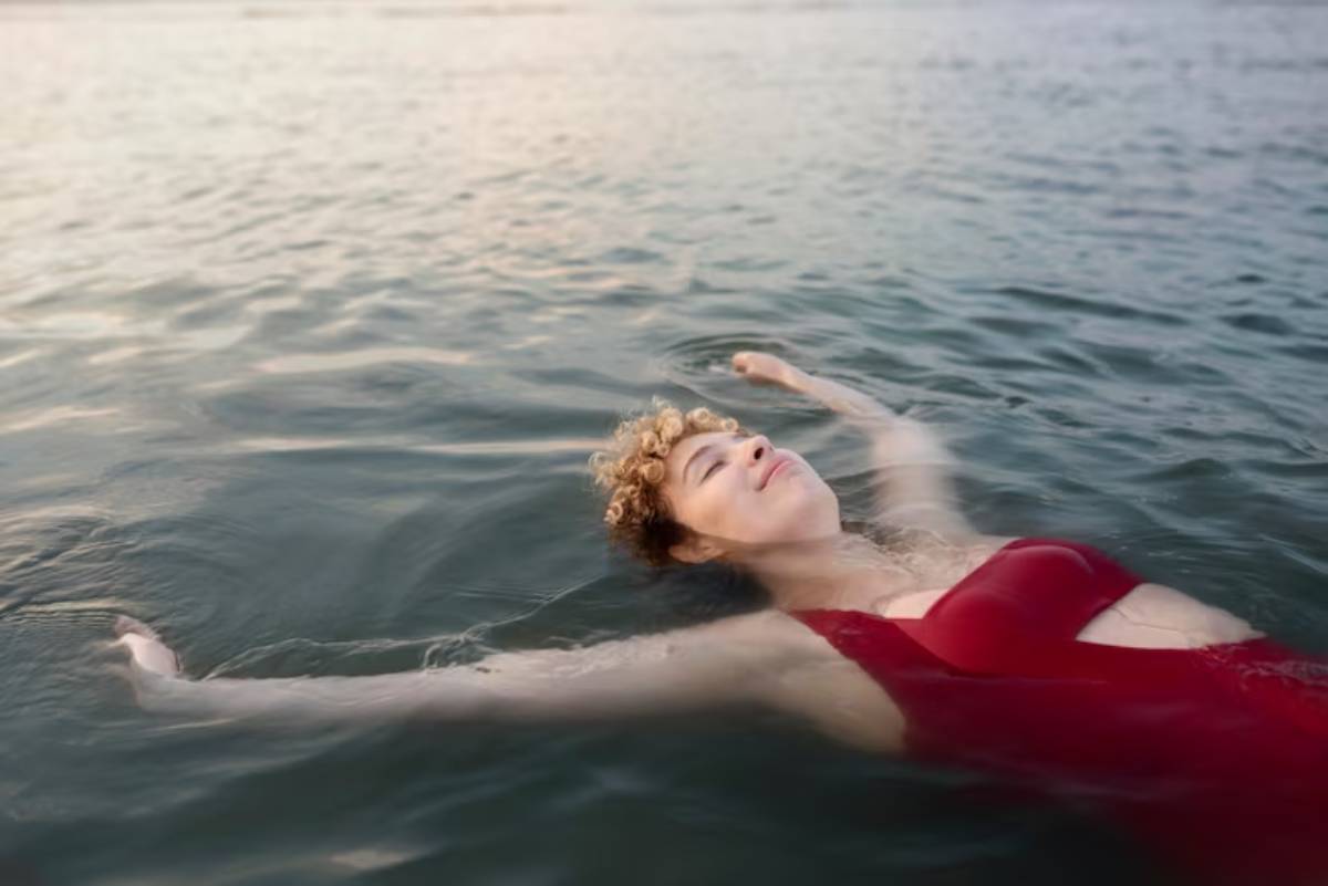 A person in a red swimsuit floats serenely on the water's surface, surrounded by gentle ripples and a soft, sunlit atmosphere.