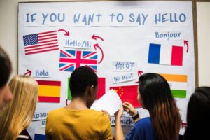 A diverse group of students reads a multilingual "Hello" poster featuring various languages and flags.