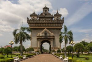 The Patuxai monument in Vientiane, Laos, stands majestically amidst lush gardens under a cloudy sky.