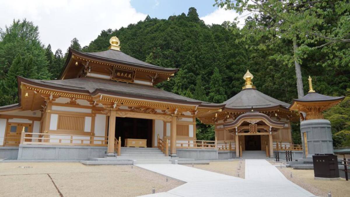 A serene Japanese temple complex with golden roofs, surrounded by lush green trees and a clear blue sky.